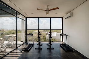 A gym with exercise equipment, large windows, and a ceiling fan.