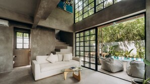 Un intérieur moderne avec un canapé blanc, une table basse en verre et une vue sur une piscine et un espace verdoyant.