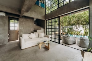 A modern interior with a white sofa, a glass coffee table, and a view of a pool and greenery.