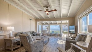 A spacious living room with a wooden floor, large windows, and a ceiling fan.