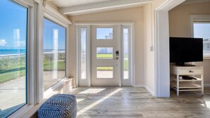 A room with a large window, a door leading outside, and a television on a wooden stand.