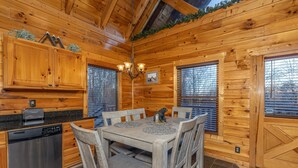 Interior de una cabaña de madera con una mesa de comedor, sillas, una lámpara de araña y un lavavajillas.