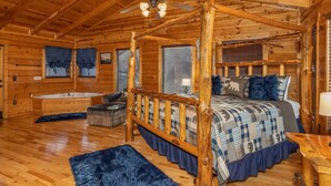 Un dormitorio de cabaña de troncos con una cama con dosel, un ventilador de techo de madera y un amplio ventanal con persianas.