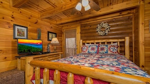 A cozy log cabin bedroom with a wooden bed, a television, and a fireplace. - A Bear's View-Gatlinburg, Resort Setting, Sleeps 6 (GATLINBURG)
