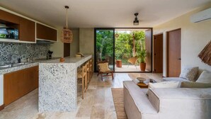 A modern kitchen with a marble island, wooden cabinets, and a dining area with chairs. There is a sliding glass door leading to a balcony with potted plants.