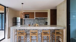 A kitchen with a marble island, wooden chairs, and a hanging light fixture.
