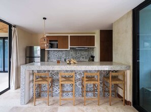 Una cocina con una isla de mármol, sillas de madera y una lámpara colgante.