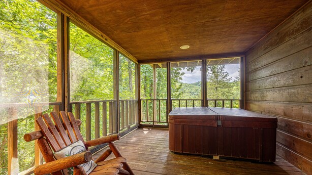 A wooden deck with a hot tub and a rocking chair, overlooking a forested area. - A Getaway With A View-Secluded Near Gatlinburg (SEVIERVILLE)