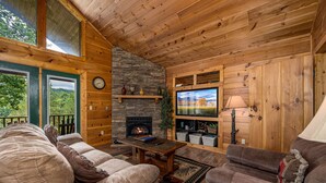 A cozy cabin interior with a stone fireplace, wooden walls, and a large TV. - A Getaway With A View-Secluded Near Gatlinburg (SEVIERVILLE)
