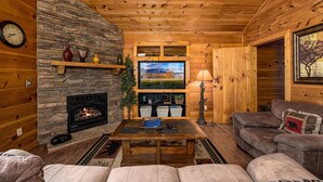 A cozy log cabin interior with a stone fireplace, wooden walls, a television, and comfortable seating. - A Getaway With A View-Secluded Near Gatlinburg (SEVIERVILLE)
