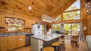 A wooden cabin interior with a kitchen, bar area, and large windows.