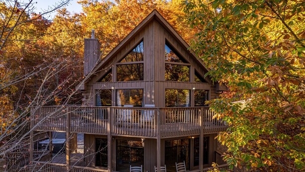 A wooden cabin with a balcony and multiple windows, surrounded by autumn foliage.