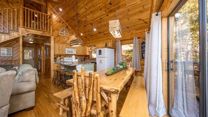 A wooden cabin interior with a dining area, kitchen, and a cozy seating space.