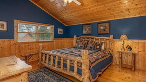 A log cabin bedroom with a wooden bed, a ceiling fan, and a rustic wooden table. - Game Room*Families Welcome*Large Hot Tub*Easy Access Roads (PIGEON FORGE)