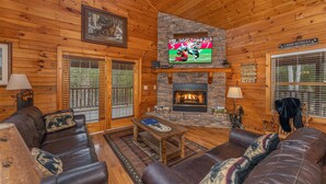 A cabin interior with a stone fireplace, leather sofas, a television, and a sign indicating a cabin retreat. - Game Room*Families Welcome*Large Hot Tub*Easy Access Roads (PIGEON FORGE)