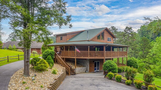 A two-story log cabin with a balcony, a stone staircase, and a flag. - Game Room*Families Welcome*Large Hot Tub*Easy Access Roads (PIGEON FORGE)