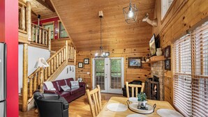 A wooden cabin interior with a dining area, a staircase, and a fireplace. - Friends/Couples*Game room w/ poker table*Close to everything (PIGEON FORGE)
