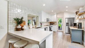 Una cocina moderna con armarios blancos, una isla grande con taburetes y vistas al exterior.