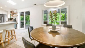 Una cocina moderna con armarios blancos, horno empotrado y microondas. Hay una zona de comedor con una mesa redonda, sillas y una planta en maceta.