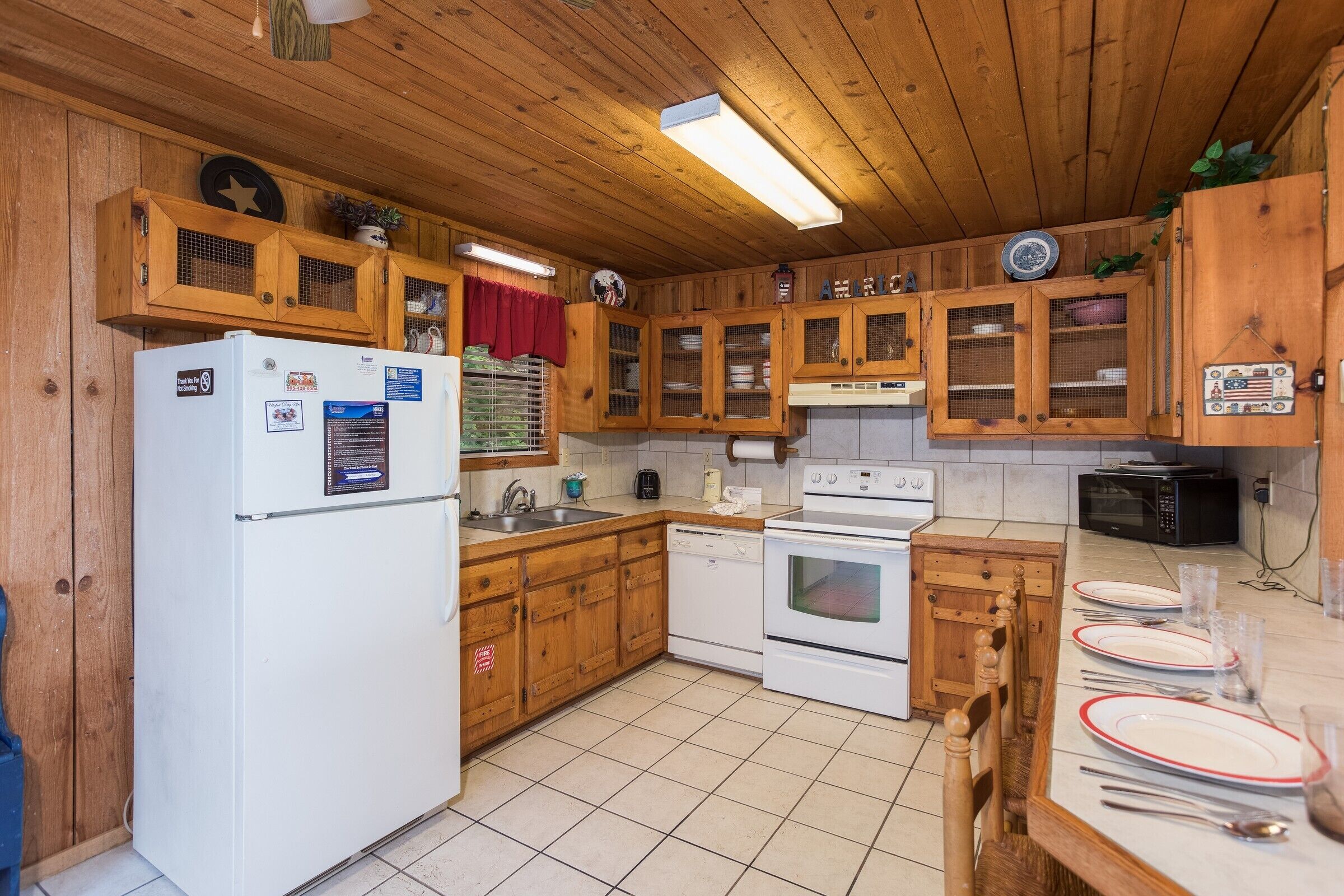 Eine Küche mit Holzschränken, einem Kühlschrank, einem Backofen, einer Mikrowelle und einem Esstisch, gedeckt mit Tellern und Besteck.