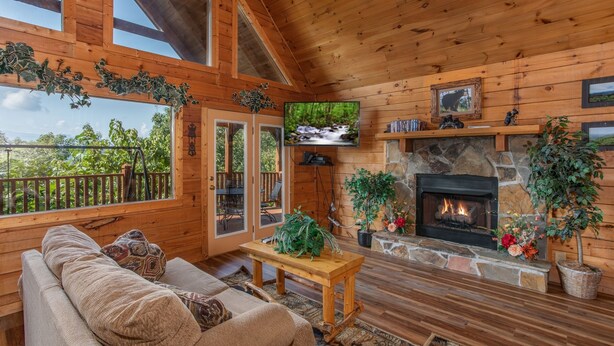 A cozy wooden cabin interior with a stone fireplace, a comfortable sofa, and a television mounted on the wall. - Angel's Majestic View*Close to Dollywood*Game Room (SEVIERVILLE)