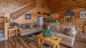 A cozy log cabin interior with a staircase, two sofas, a dining table, and a kitchen area. - Angel's Majestic View*Close to Dollywood*Game Room (SEVIERVILLE)