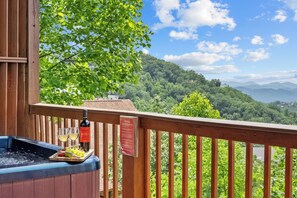 A hot tub with a wooden deck, a bottle of wine, and a tray with grapes.
