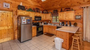 A cabin-style kitchen with wooden cabinets, a stainless steel refrigerator, a microwave, and a stove. There is a wooden island with stools and a trash bin. - Easy Access Roads*In Pigeon Forge*Jacuzzi and hot tub (PIGEON FORGE)