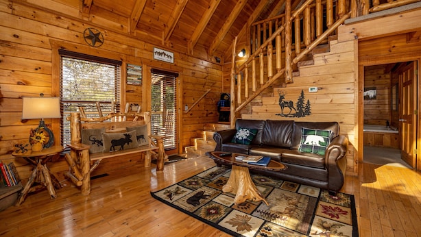 Interior de una cabaña de troncos con escalera de madera, un sofá de cuero y decoración rústica.