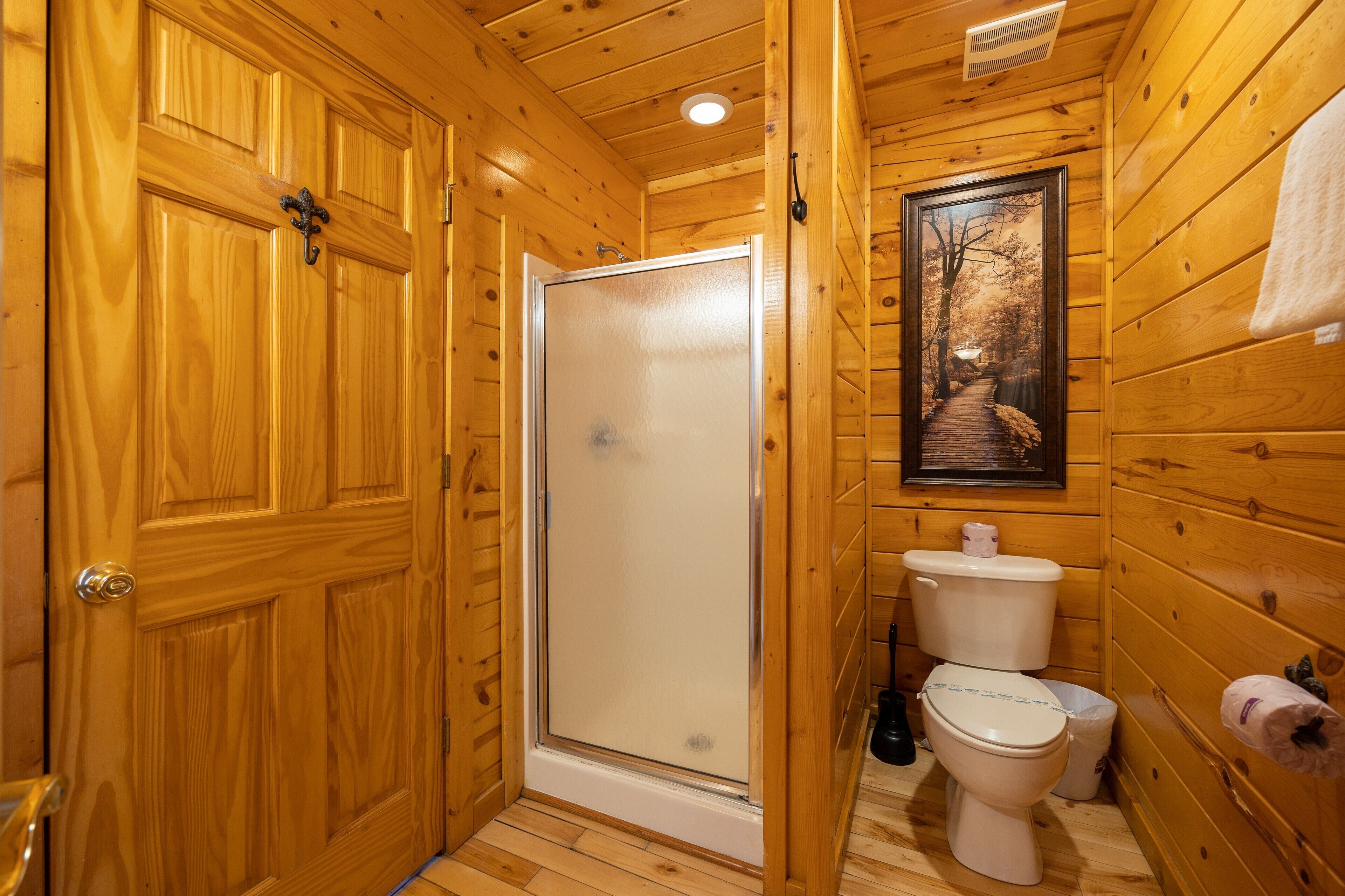 Un baño de madera con ducha, inodoro y un cuadro enmarcado en la pared.