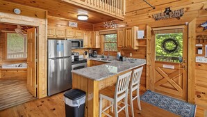 A cabin-style kitchen with wooden cabinets, a stainless steel refrigerator, a sink, and a breakfast bar.