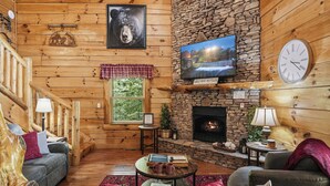A log cabin interior with a stone fireplace, wooden walls, a television, and a clock. - Resort*Luxury*Close to Pigeon Forge*Game Loft*Seasonal Pool (SEVIERVILLE)