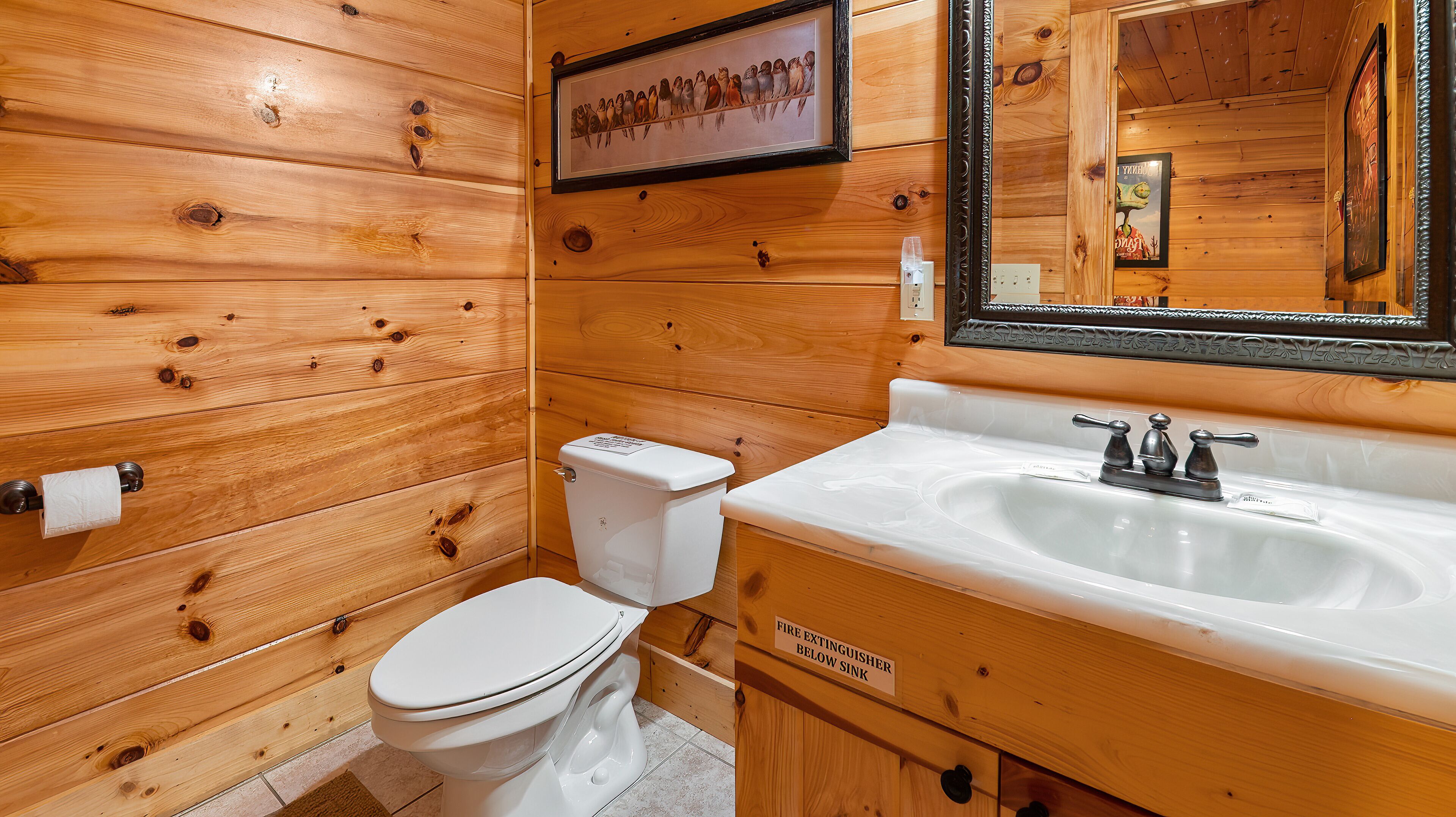 Un bagno in una cabina di legno con toilette, lavabo e un quadro appeso raffigurante degli uccelli.
