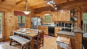 A wooden cabin interior with a dining table, chairs, a kitchen with granite countertops, and a refrigerator. - Resort*Luxury*Close to Pigeon Forge*Game Loft*Seasonal Pool (SEVIERVILLE)