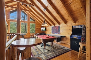 L’intérieur d’un chalet en bois comprend une table de billard, un jeu de billard, une table de ping-pong et une console de jeux vidéo.