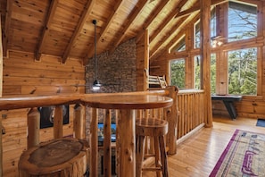 A wooden interior with a bar area, stone wall, and large windows.