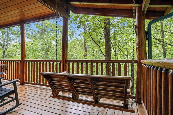 A wooden deck with a bench, a table, and a view of a forest.