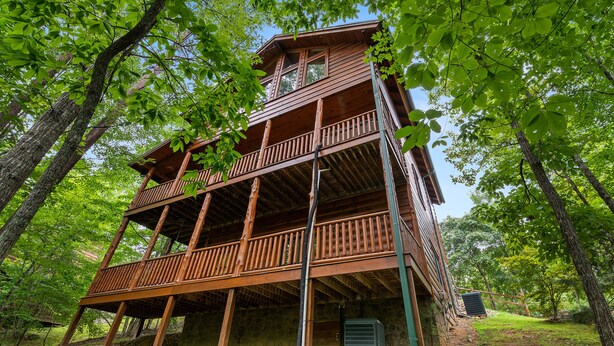 A multi-story wooden cabin with a balcony on each floor, surrounded by trees. - Resort*Luxury*Close to Pigeon Forge*Game Loft*Seasonal Pool (SEVIERVILLE)