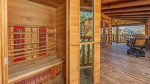 A wooden sauna with benches and a glass door, a wooden deck with outdoor seating, and a view of trees and hills. - Pigeon Forge*Mountain Views*Family Fun*Game Room*Hot Tub (PIGEON FORGE)