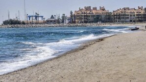 A beach with waves, a rocky breakwater, and buildings in the background.