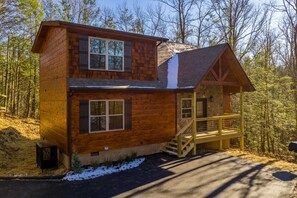 Une cabane en rondins à deux étages, dotée d’une terrasse en bois et d’un escalier menant à l’entrée.
