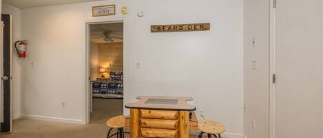 Une pièce avec une table en bois brut et deux tabourets, une enseigne indiquant « ANTRE DES OURS », et une porte portant l’inscription « VISITEURS ».