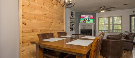 Un comedor con una mesa y sillas de madera, un ventilador de techo y un televisor al fondo.