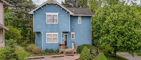 A two-story blue house with a front porch, a small deck, and a well-maintained lawn.