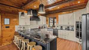 A kitchen with wooden walls, a large island with stools, and modern appliances. - Wears Valley*Mtn Views*Tons of Great Amenities*Gated Resort (PIGEON FORGE)
