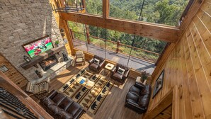 A spacious living area with a stone fireplace, leather sofas, and a large window overlooking a forest. - Wears Valley*Mtn Views*Tons of Great Amenities*Gated Resort (PIGEON FORGE)