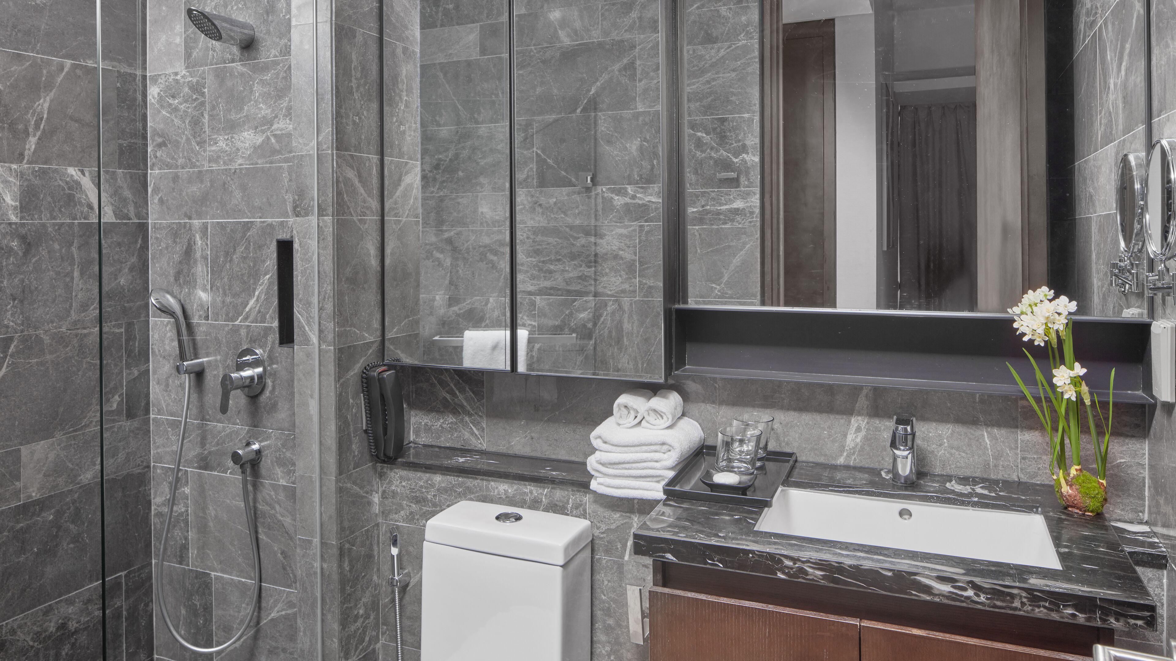 A modern bathroom with a marble shower, a sink, and a mirror.