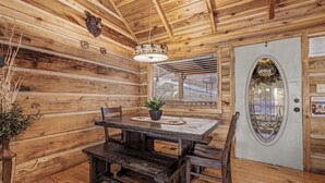 Interno di una baita in legno con un tavolo da pranzo, panche, una pianta in vaso e una porta decorativa.