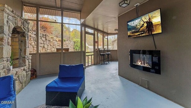 A spacious indoor area with a stone fireplace, a television mounted on the wall, and a comfortable seating area with blue cushions. - House in Gatlinburg*Private Outdoor Pool*Fire Pit*Pool Table (GATLINBURG)