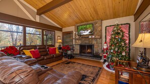 A cozy living room with a leather sofa, a fireplace, a Christmas tree, and a television mounted on a stone wall.